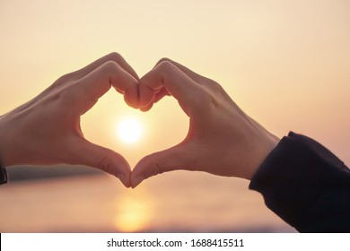 Woman Hand Do Heart Shape On Sunset Sky And Bokeh Background.