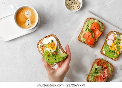 Woman hand eating a toast with avocado and egg, micro greens. Set of sandwiches with different toppings - salmon, hamon. Morning, coffee, breakfast - Powered by Shutterstock