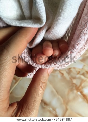 A woman hand gently touching a baby’s tiny toes  covering under a white cloth.