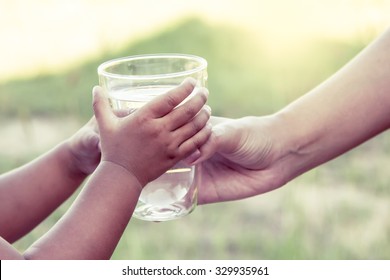 Woman Hand Giving Glass Of Fresh Water To Little Child Girl In The Park,vintage Color Filter