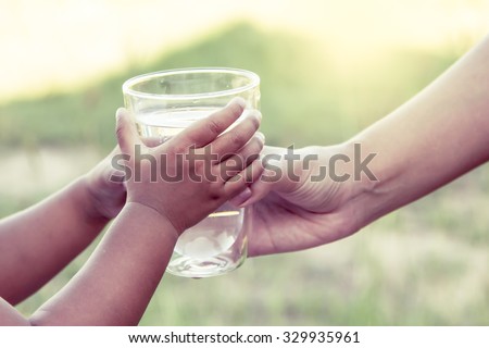 Woman hand giving glass of fresh water to little child girl in the park,vintage color filter