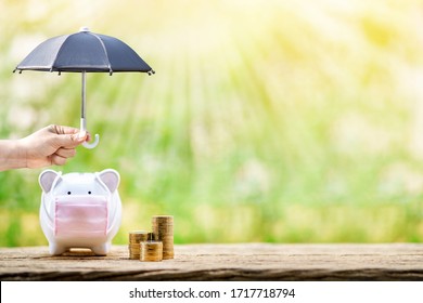 Woman hand hold the black umbrella for protect to sick piggy bank wearing surgical mask to prevent viruses and diseases put beside three stack gold, Saving money for buy health insurance concept. - Shutterstock ID 1717718794
