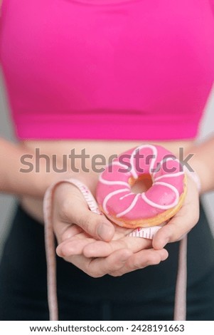 woman hand hold Donut with tape measure, choose stop eating sweet is Unhealthy ealthy food. Dieting control, Weight loss, Obesity, eating lifestyle and nutrition concepts