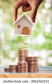 Woman Hand Hold A Home Model Present To Stack Gold Coin With Growing Value Put On The Wood In The Public Park, Loan Or Save Money For Buy Real Estate To Family Concept.