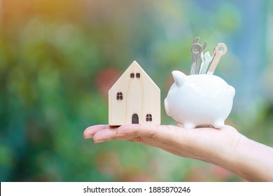 Woman Hand Hold Piggy Bank With Grow Increase Value And Wrench Tools With Build And New House In The Public Park, Saving Money And Loan For Construction Real Estate Concept.