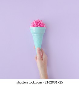 Woman hand hold pink paper ice cream scoop with ice cream plastic cone on pastel purple background. Minimal summer concept. Micro plastic in food. Recycling.