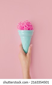 Woman hand hold pink paper ice cream scoop with ice cream plastic cone on pastel pink background. Minimal summer concept. Micro plastic in food. Recycling.