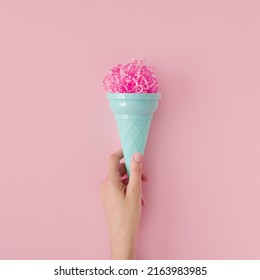Woman hand hold pink paper ice cream scoop with ice cream plastic cone on pastel pink background. Minimal summer concept. Micro plastic in food. Recycling.