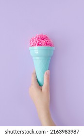 Woman hand hold pink paper ice cream scoop with ice cream plastic cone on pastel purple background. Minimal summer concept. Micro plastic in food. Recycling.