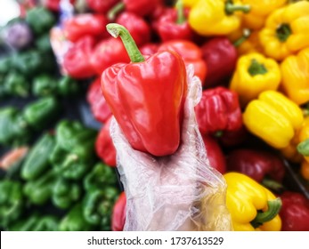 Woman hand hold red bell pepper with plastic glove in supermarket. Safety and Health concept for prevent virus Covid-19. Selective focus. - Powered by Shutterstock