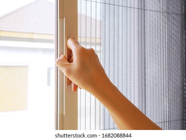 Woman hand hold retractable pleated insect screen holder to open or close the window ,selective focus on the hand