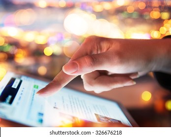 Woman Hand Hold And Touch Screen Tablet On Abstract Blurred Bokeh Of City Night Light Background. Focus In The Foreground.