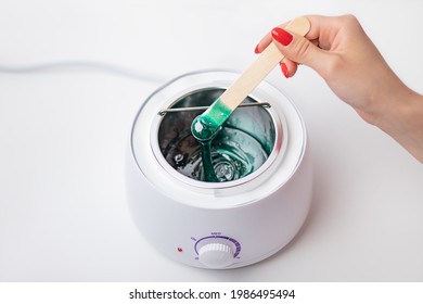 Woman Hand Hold Wooden Spatula For Depilation And Stir Hot Wax In Thermostat Heater. Hair Removal Concept On White Background.