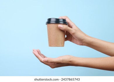 Woman hand holding blank coffee paper cup for mockup isolated over blue background