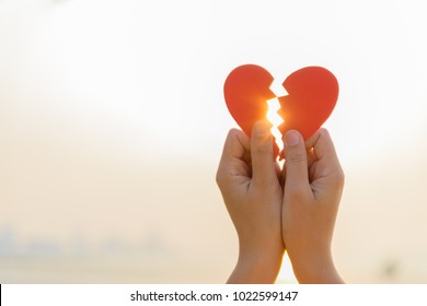 Woman hand holding broken paper red heart on sunset. Love, Wedding and Valentines day concept.