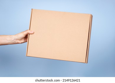 Woman hand holding brown ecological package box made of natural corrugated cardboard. Mockup mailing parcel box on blue background. Packaging, shopping, delivery concept