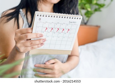 woman hand holding calendar with question mark waiting for late blood period, amenorrhea, irregular periods concept 