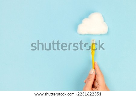 Woman hand holding connection cable towards the cloud on blue background. Internet connection and cloud technology.
