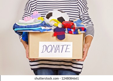 Woman hand holding donation box with clothes, toys and books for charity - Powered by Shutterstock