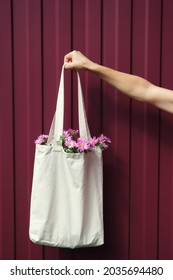 Woman Hand Holding Eco Reusable Blank Canvas Shopping Bag With Flowers Inside On Red Background. Zero Waste Mock-up. Vertical. 