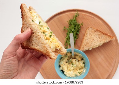 Woman Hand Holding Egg Salad Sandwich With Whole Wheat Toasted Bread On White Background. Healthy Breakfast Concept. POV Point Of View