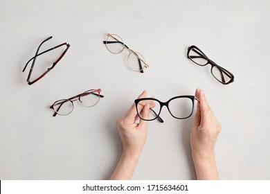 Woman hand holding eyeglasses. Optical store, glasses selection, eye test, vision examination at optician, fashion accessories concept. Top view, flat lay