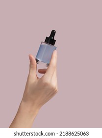 Woman hand holding facial essential oil or serum packaging on pink background. Beauty cosmetic product for skincare concept. Mockup. High quality photo