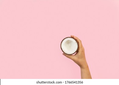 Woman hand holding halved coconut on a pink background with copy space