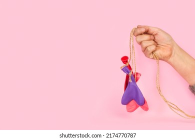 Woman Hand Holding Heart Shape Deflated Colored Balloons Tied With Sisal Yhreads On A Pink Background With Copy Space