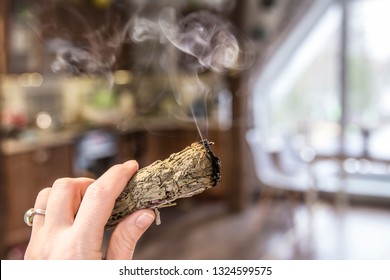 Woman Hand Holding Herb Bundle Of Dried Sage Smudge Stick Smoking. It Is Believed To Cleanse Negative Energy And Purify Living Spaces At Home In Rooms.