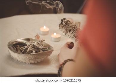 Woman hand holding herb bundle of dried sage smudge stick smoking