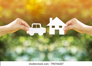 Woman Hand Holding Home And Car With Paper Art Filed Together On Bokeh Background In The Public Park, Loans For Buying A House Vs Buying A Car Before Anything Good Concept.