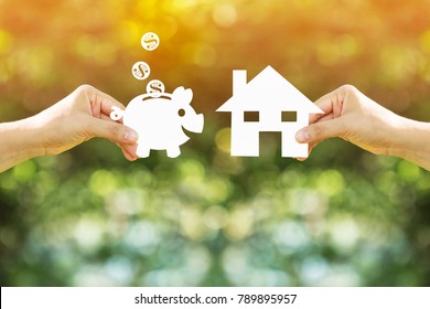 Woman hand holding a home and piggy bank and dollar coin model made of paper art filed together on nature bokeh in the public park, Loan or save money for buy a house and real estate concept