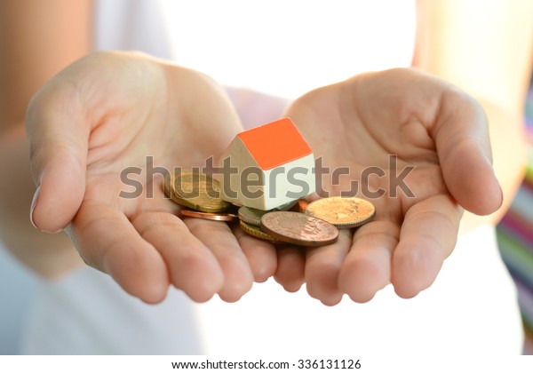 Woman hand holding house and money suggesting the\
rising cost of home\
prices