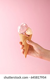 Woman hand holding an ice cream cone on a pink background. 