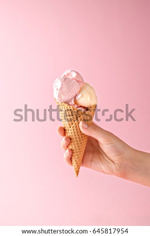 Woman hand holding an ice cream cone on a pink background. 