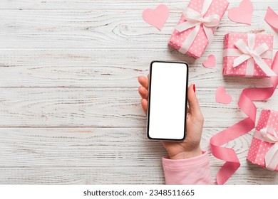 Woman hand holding mobile phone with blank screen on colored background with hearts, valentine day concept top view flat lay.