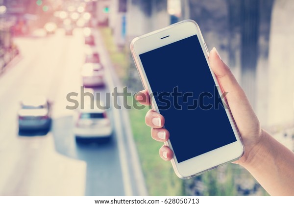 Woman\
hand holding mobile smart phone isolated black screen with car on\
road, mock up for advertising design or\
backgrounds