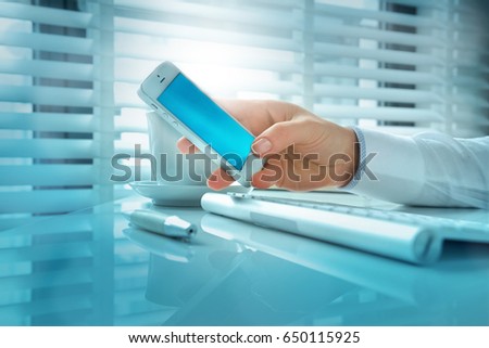 Woman hand holding a modern smartphone typing message or checking newsfeed on social media in the office with contact icons in the foreground: at, envelope, chat and smartphone