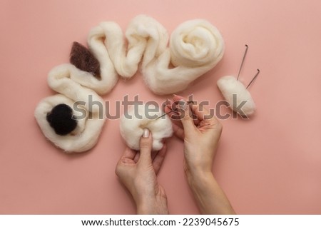 woman hand holding needle felting kit. felted woolen needle and skein of wool on pink table, flat lay