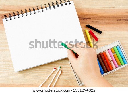 Woman hand holding oil pastel art picking for art drawing on paper and set box of colorful crayons on wood table background with copy space for text.