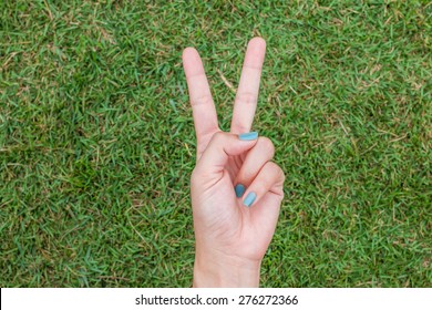 Woman Hand Holding Up The Peace Sign Or Number Two With Two Fingers On Green Grass Background Texture