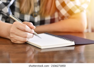 Woman Hand Holding Pen Writing On Spiral Book With Sunlight.