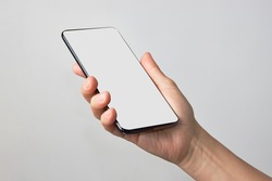 Woman Hand Holding Phone On White Background With Copy Space. Woman Holding Smartphone With White Screen. Hand With Blank Cellphone Display, Close-up