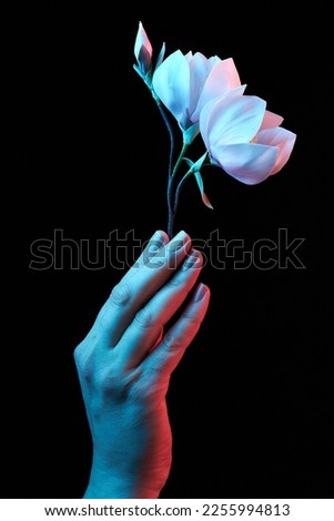 Woman hand holding pink blooming artificial magnolia flower from foamiran in neon light on dark background