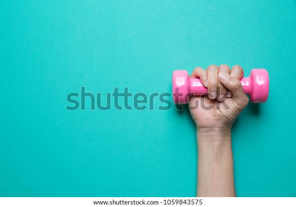 woman hand\
holding pink dumbbell on green\
background