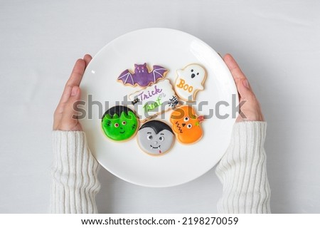 woman hand holding plate of funny Halloween Cookies. Happy Halloween day, Trick or Threat, Hello October, fall autumn, Traditional, party and holiday concept