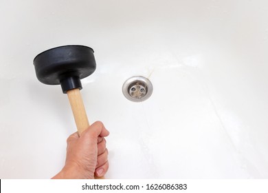 Woman hand holding a plunger to clean bathtub drain, sewer clogged, blocked with fallen out hair.