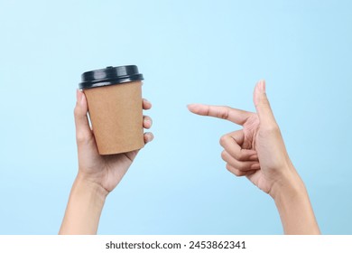 Woman hand holding and pointing finger to blank coffee paper cup for mockup isolated on blue background