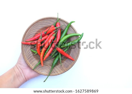 woman hand holding red and green hot chilli on a wooden plate